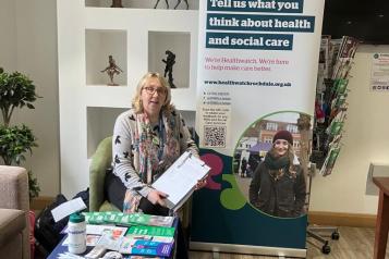 Community Project Worker sat in front of a Healthwatch banner at Hare Hill Cafe