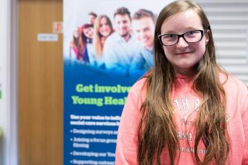 Teenage girl wearing glasses in front of a Healthwatch banner