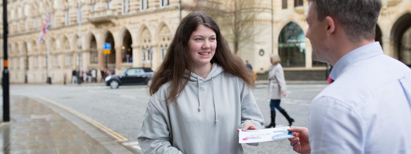 Young female volunteer handing out a leaflet to a male member of the public