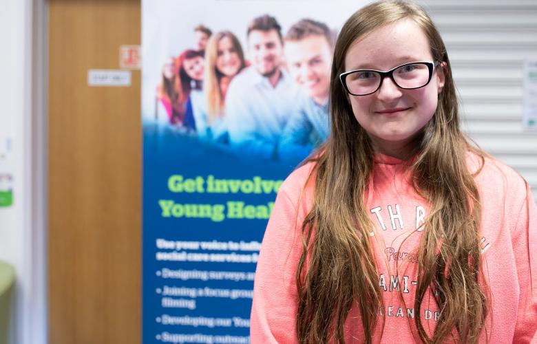 Teenage girl wearing glasses in front of a Healthwatch banner